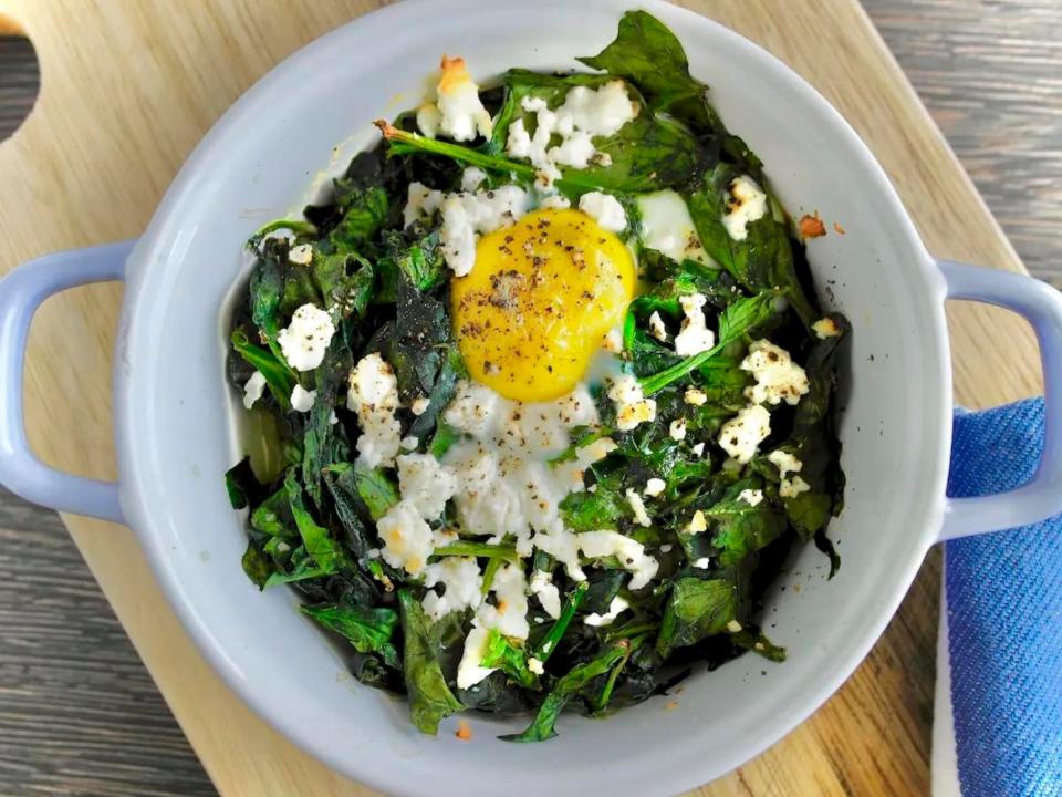A bowl of baked spinach, feta, and eggs on a wooden chopping board.