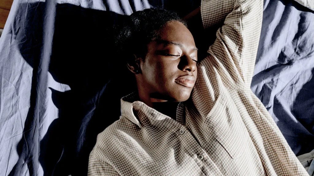 black person in chequered brown pyjamas asleep on bed
